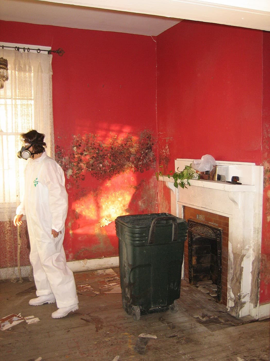 Person in a white disposable coverall and full-face respirator standing in a room with heavy mold growth on the wall