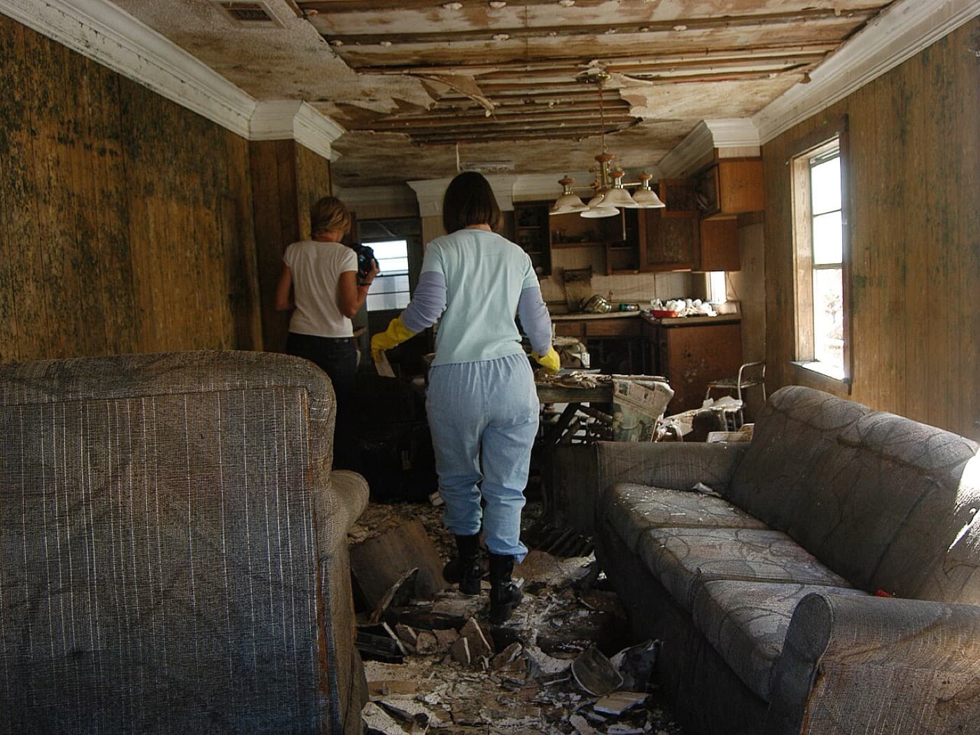 Living room with mold covering the walls, a collapsed ceiling, and mold-damaged upholstered furniture