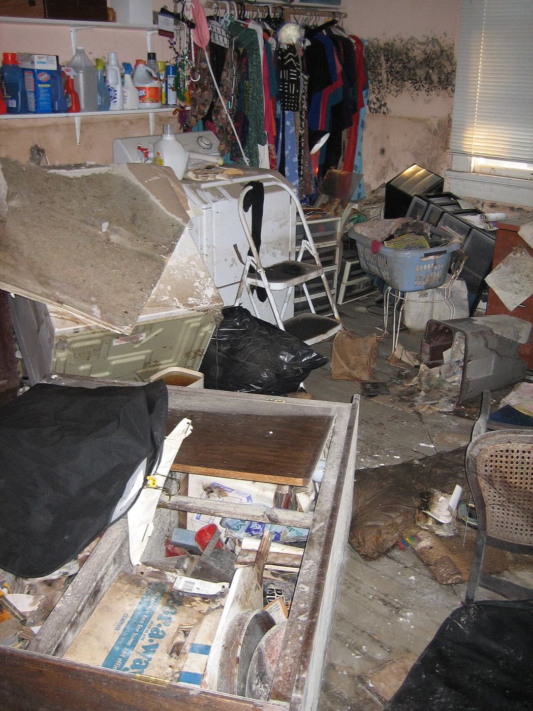Cluttered basement utility room with mold growth across the upper walls near the ceiling