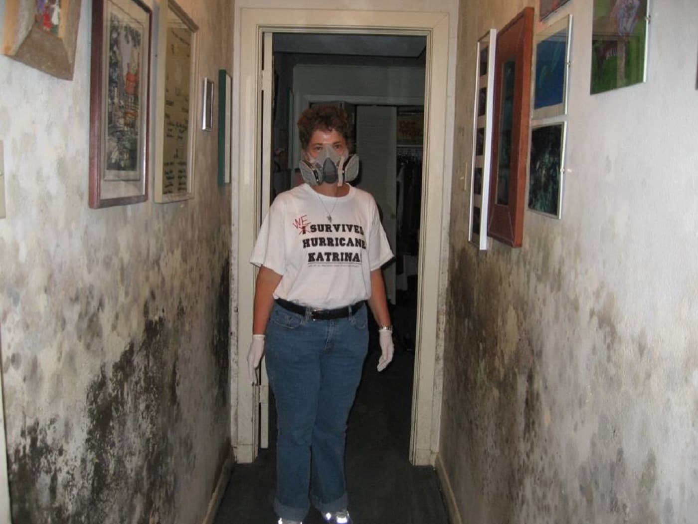 Person wearing a half-face cartridge respirator and gloves in a hallway with mold covering both walls
